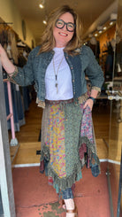 Woman standing in a store doorway wearing a patterned dress and denim jacket.
