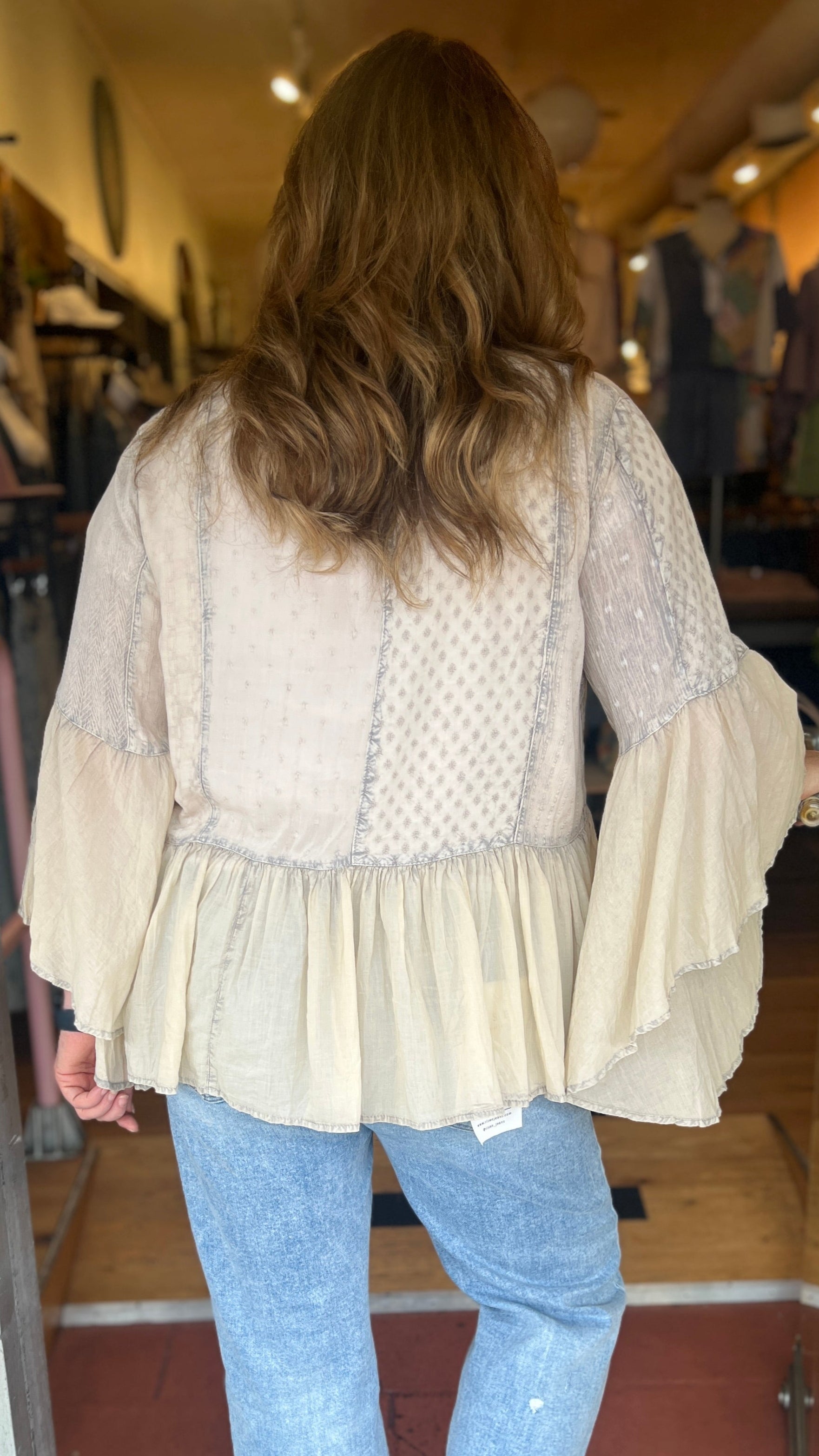 Woman wearing a light blouse and jeans entering a store.