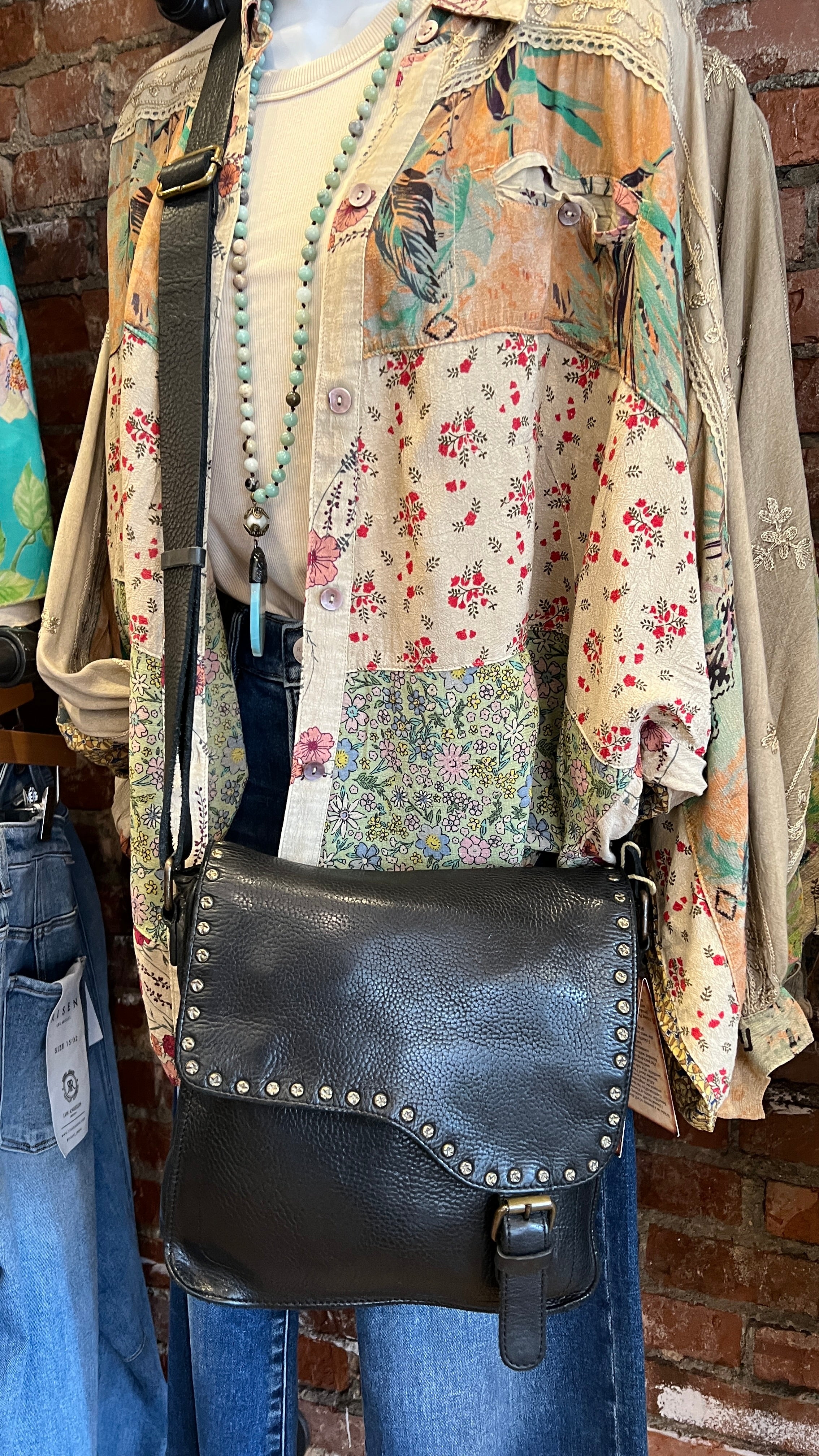 Black leather bag with studs on a mannequin against a brick wall.