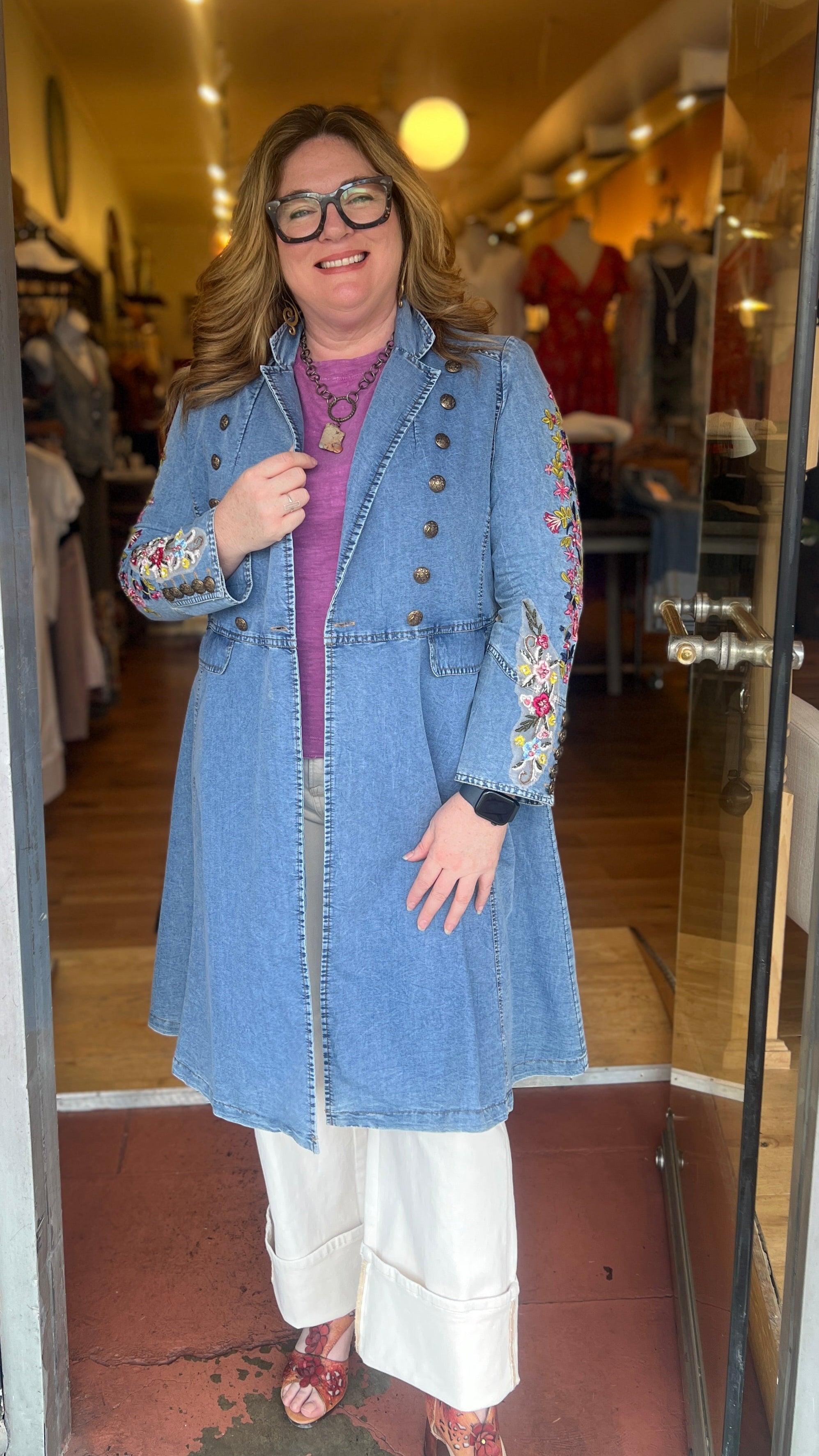 Woman wearing a blue denim coat with floral embroidery in a store setting