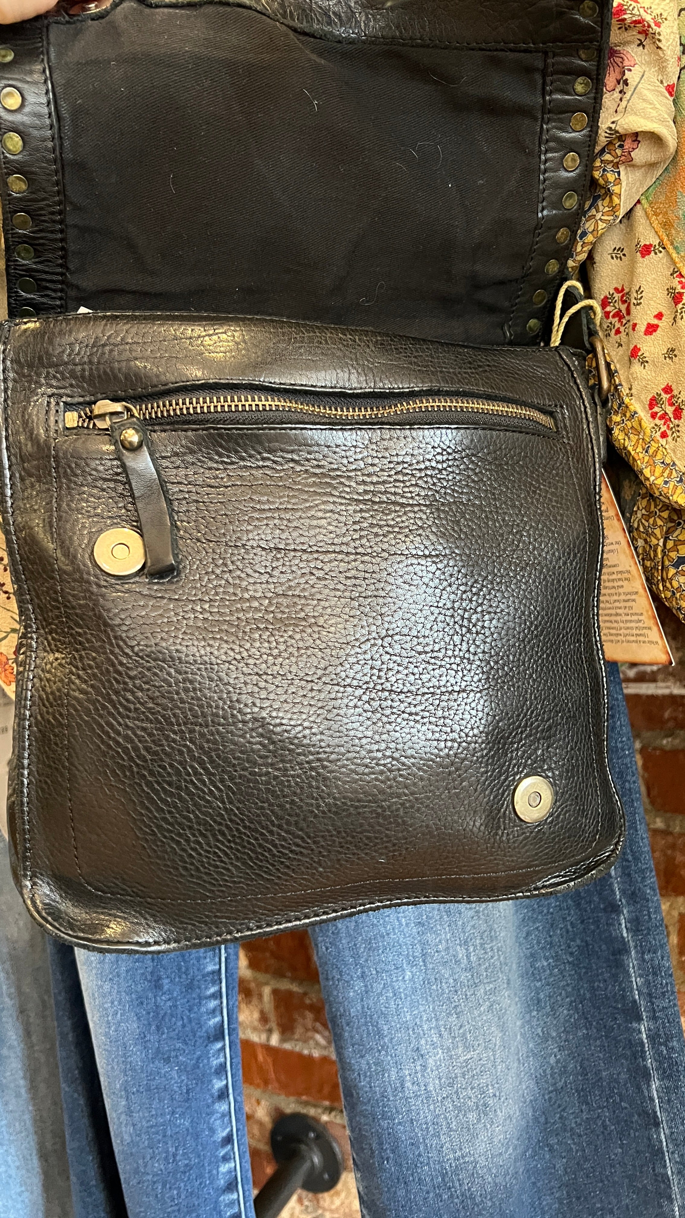 Black leather bag held by a person wearing jeans, with a patterned background.