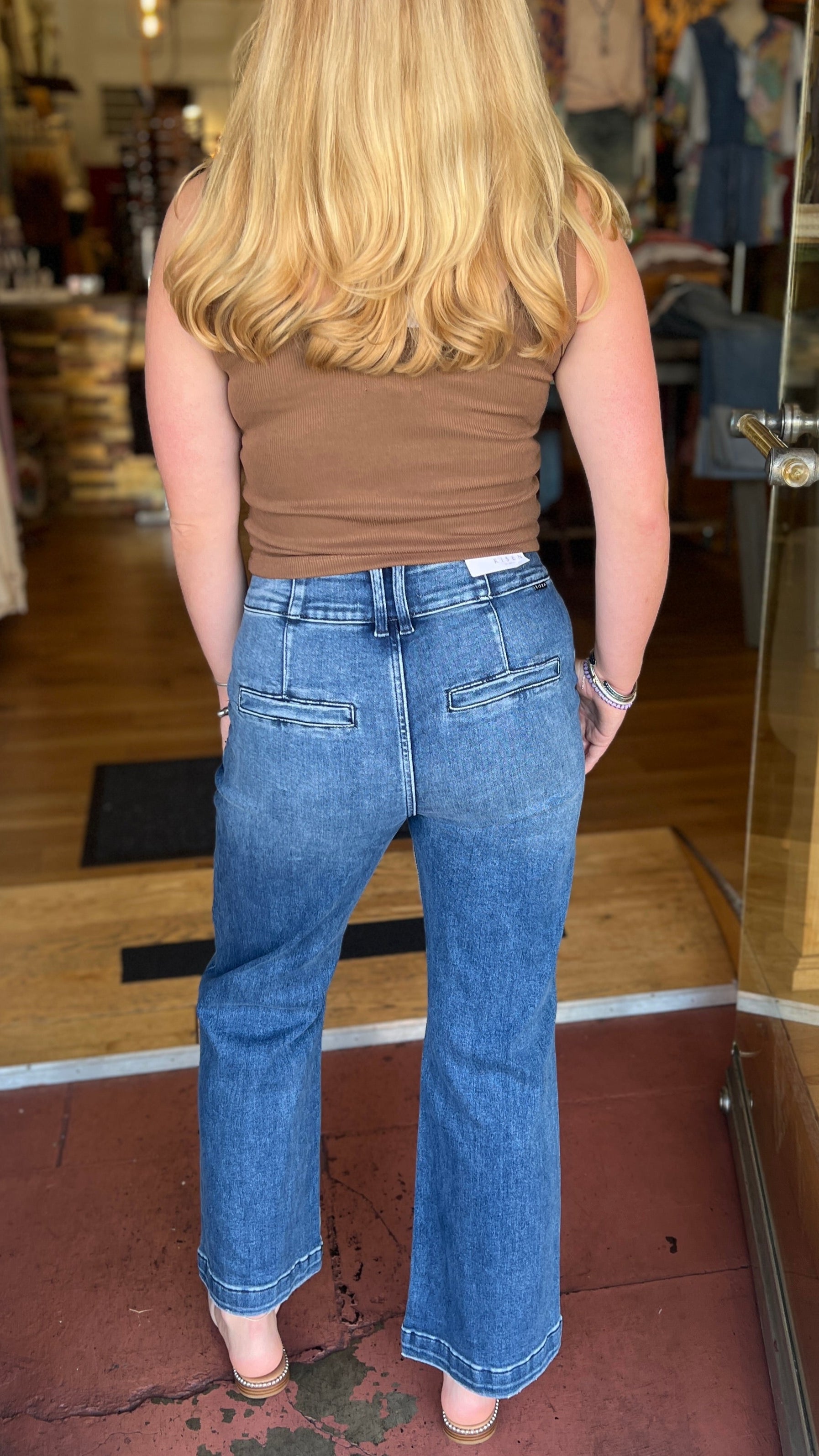 Person wearing a brown top and blue jeans standing in a store doorway.