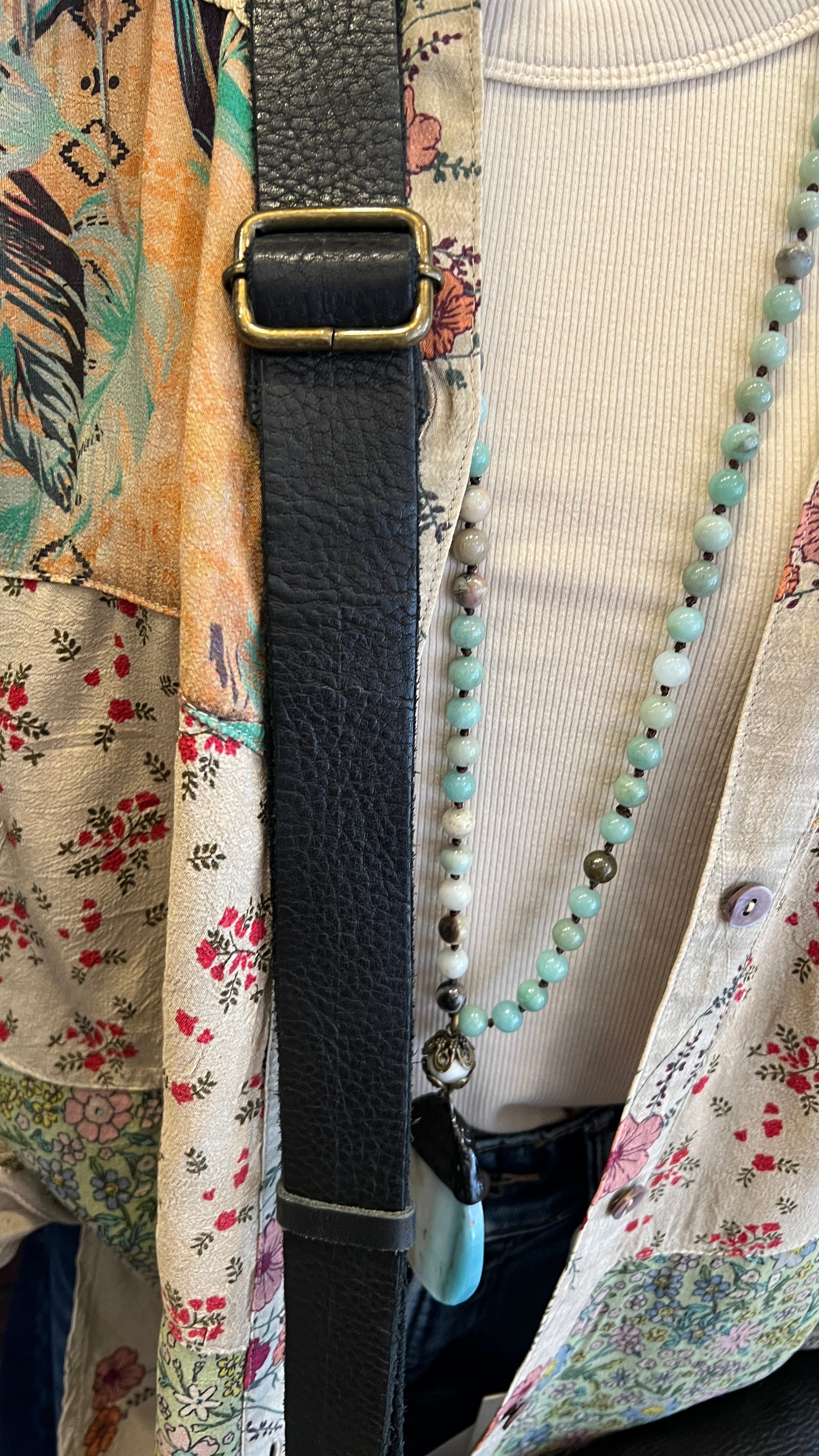 Close-up of a black strap with a gold buckle on a floral-patterned garment.