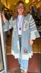 Woman standing in a store doorway wearing a long, patterned cardigan.