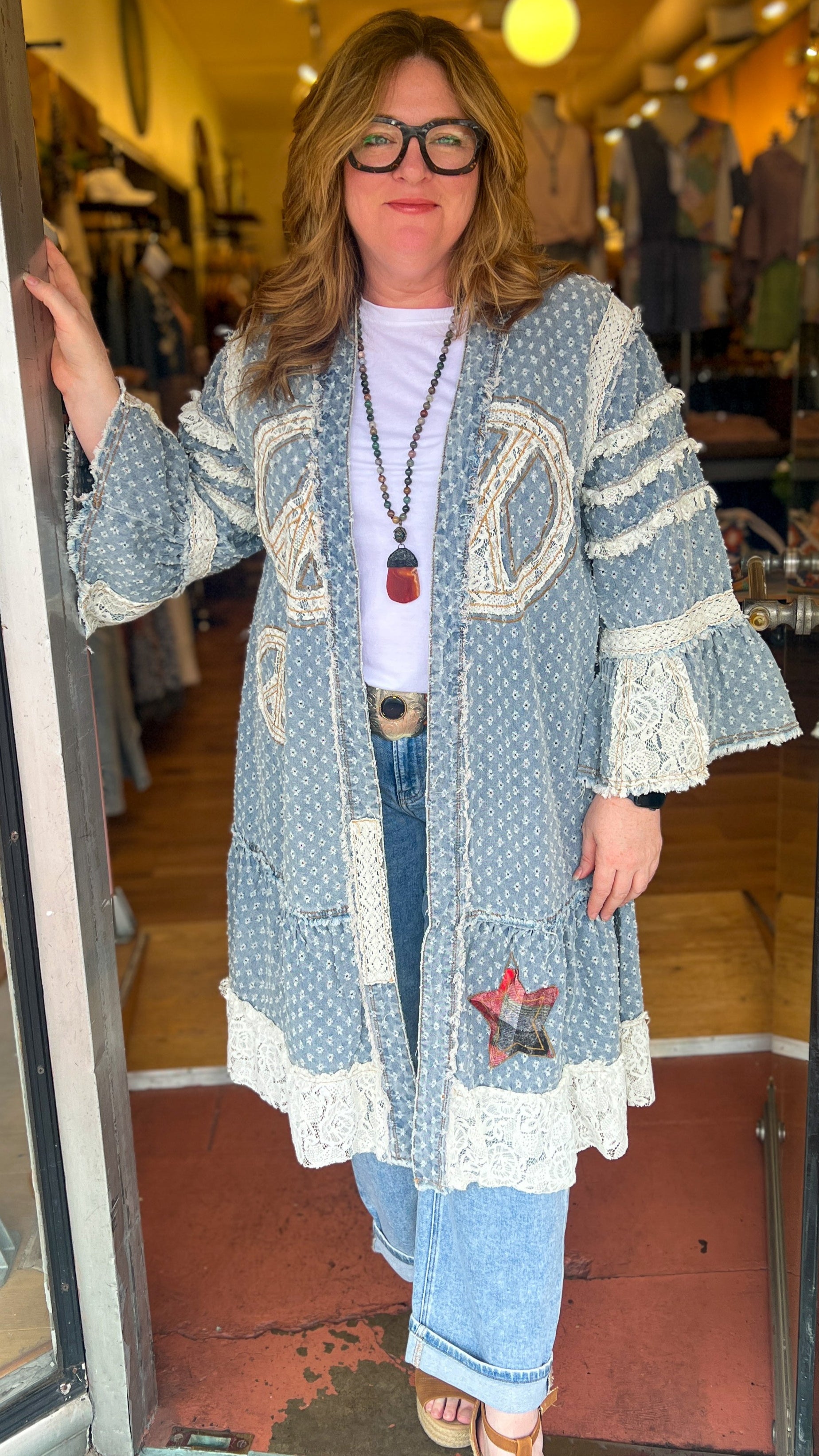 Woman standing in a store doorway wearing a long, patterned cardigan.