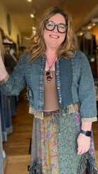 Woman standing in a store doorway wearing a denim jacket and colorful skirt.