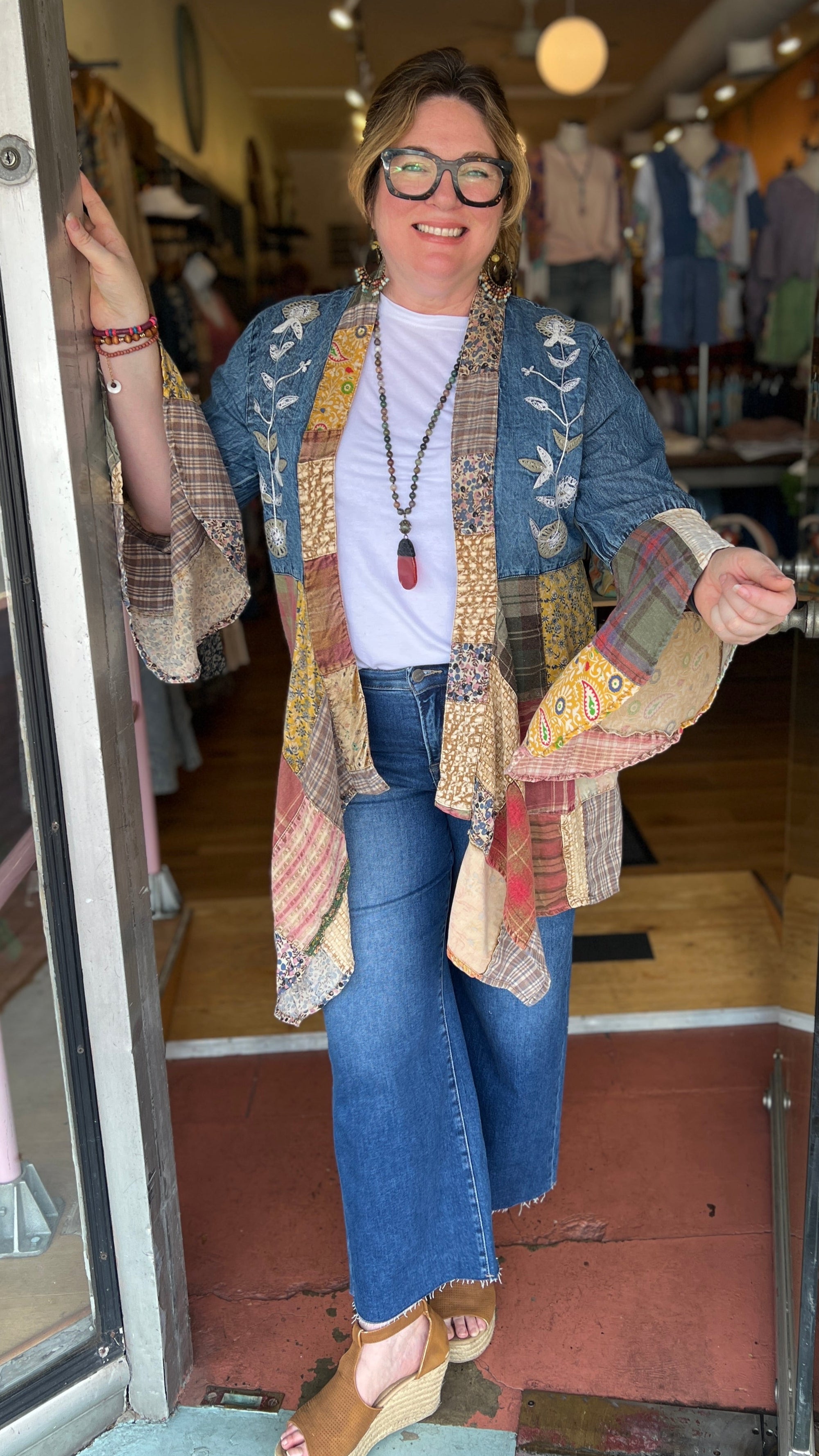 Woman standing in a store doorway wearing a colorful patterned cardigan, smiling.