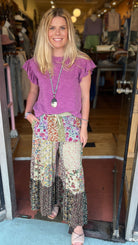 Woman in a purple top and floral pants standing in a store doorway.