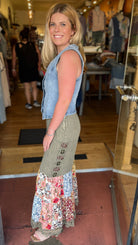 Woman standing in a clothing store wearing a denim vest and floral dress.