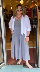 Woman standing in front of a store window wearing a white jacket and gray dress.