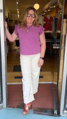 Woman in a purple shirt and white pants standing in front of a store entrance.