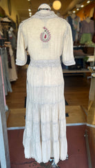 Vintage-style white dress with intricate detailing on a mannequin in a store setting.