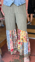 Person wearing green pants with floral patchwork at the bottom in an indoor setting.
