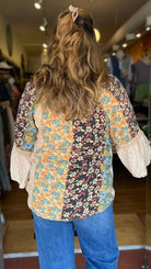 Person wearing a patterned shirt and blue jeans entering a store.