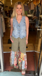 Woman standing in a store doorway wearing a denim vest and patterned pants.