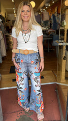 Woman standing in a clothing store wearing a white t-shirt, floral pants, and a brown belt.