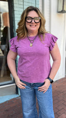 Woman wearing a purple shirt and blue jeans standing on a sidewalk.