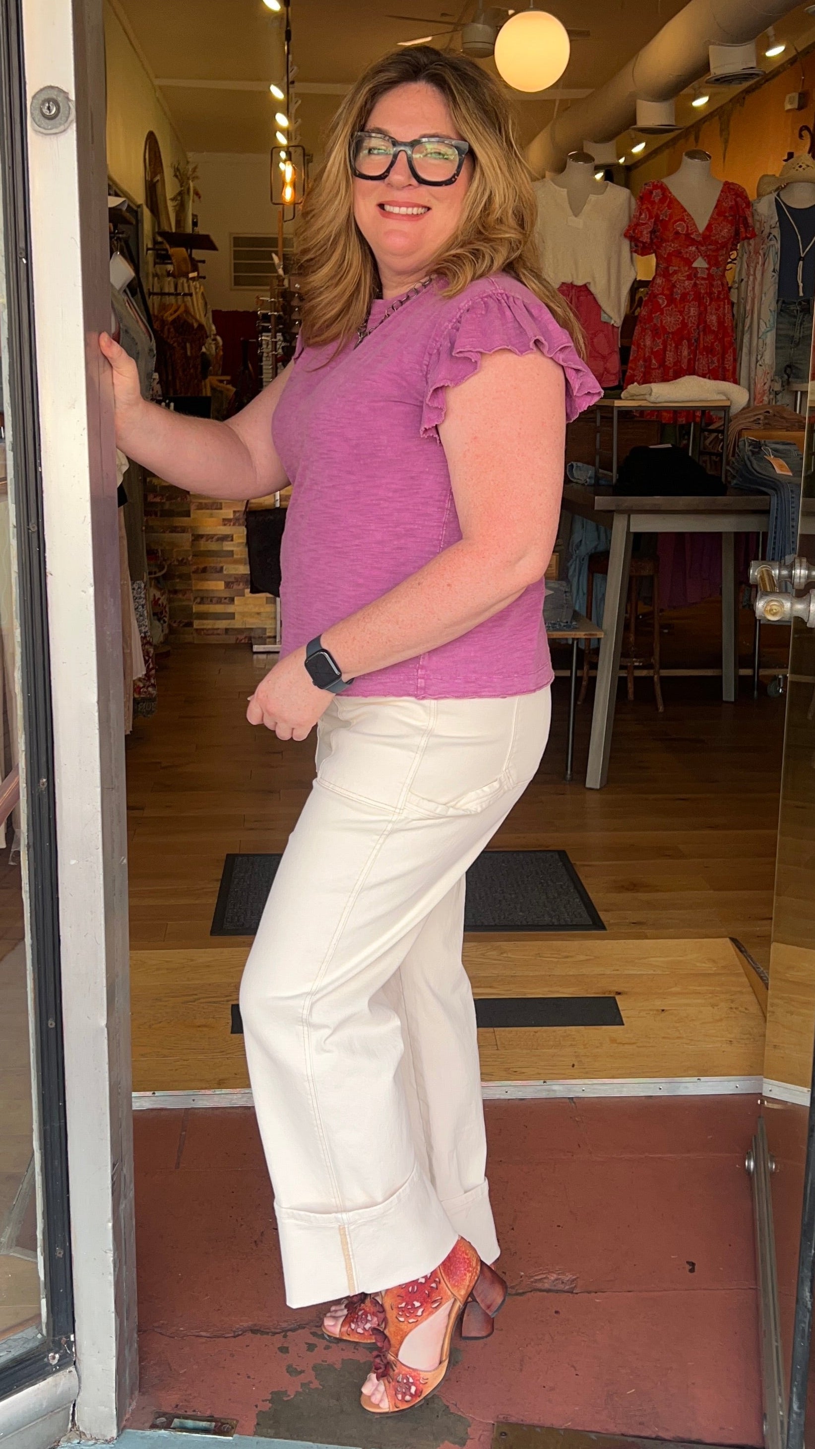 Woman in a pink shirt and white pants standing in a store doorway.