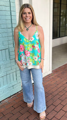 Woman wearing a floral top and jeans standing on a brick sidewalk.