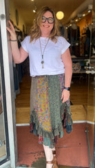 Woman standing in front of a store entrance wearing a white t-shirt and patterned skirt.
