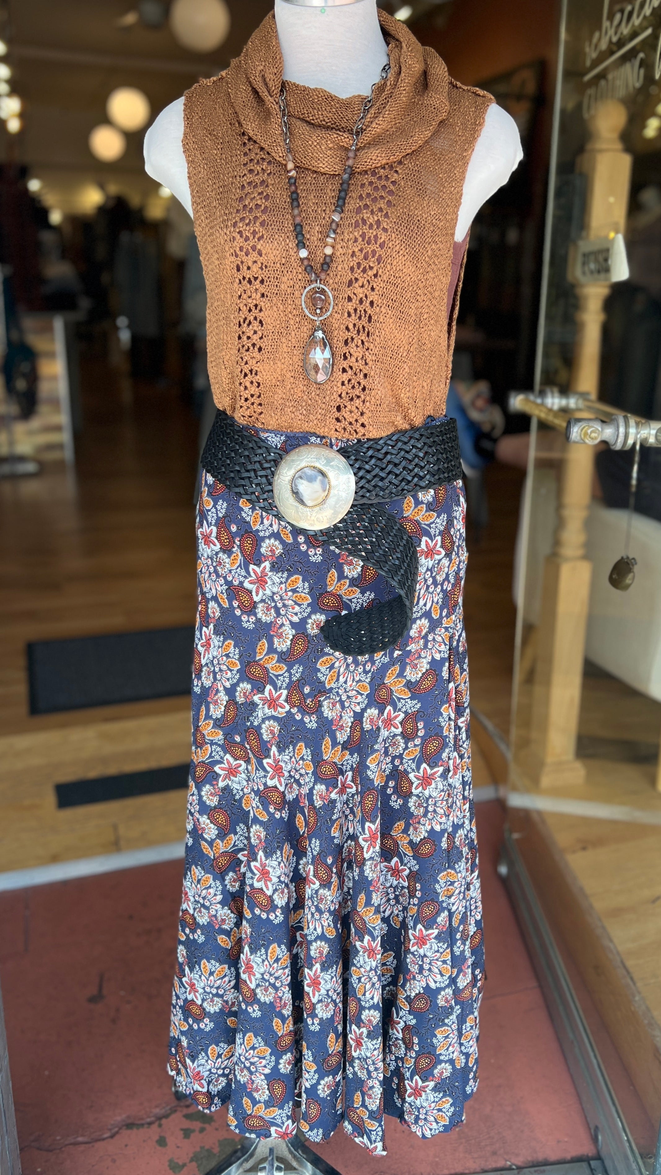 Mannequin wearing a brown sleeveless top and floral dress with a belt in a store setting.