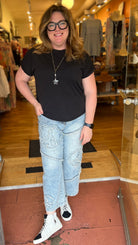Woman standing in a clothing store wearing a black t-shirt and light blue jeans.